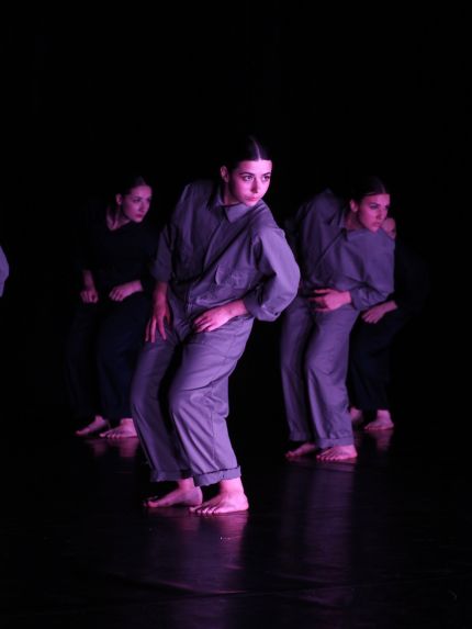 Drei Tanzende stehen parallel zueinander, pink angeleuchtet, in Blaumännern und neigen sich zur Seite